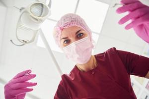 giovane femmina dentista nel protettivo maschera Lavorando nel stomatologia clinica. primo persona Visualizza foto