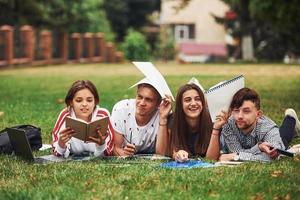 annoiato e avendo divertimento. gruppo di giovane studenti nel casuale Abiti su verde erba a giorno foto