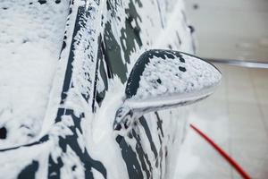 maschio lavoratore nel uniforme lavaggio nuovo moderno auto quello coperto con sapone. concezione di servizio foto