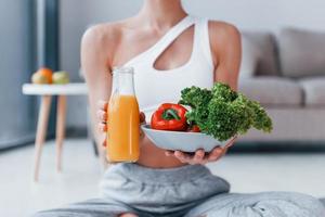 con salutare cibo e arancia succo nel mani. giovane donna con sottile corpo forma nel abbigliamento sportivo avere fitness giorno in casa a casa foto