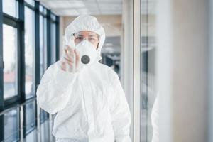 femmina medico scienziato nel laboratorio cappotto, difensiva occhiali e maschera in piedi in casa con antibatterico spray foto