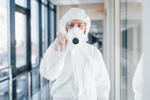 femmina medico scienziato nel laboratorio cappotto, difensiva occhiali e maschera in piedi in casa con antibatterico spray foto