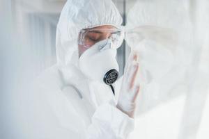 si sente cattivo e malato. femmina medico scienziato nel laboratorio cappotto, difensiva occhiali e maschera in piedi in casa foto