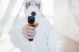 femmina medico scienziato nel laboratorio cappotto, difensiva occhiali e maschera in piedi in casa con infranto termometro foto
