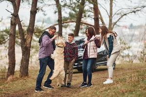 contento famiglia avere divertimento con loro attivo cane vicino moderno auto all'aperto nel foresta foto