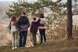 posteriore Visualizza di famiglia quello in piedi insieme con loro cane all'aperto nel foresta foto