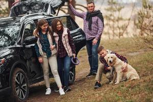 contento famiglia avere divertimento con loro cane vicino moderno auto all'aperto nel foresta foto