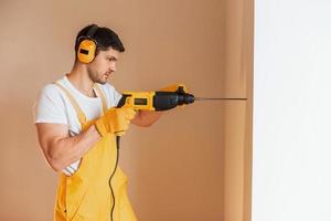 tuttofare nel giallo uniforme lavori in casa di utilizzando martello trapano. Casa rinnovamento concezione foto