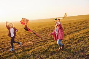 Due poco ragazze amici avere divertimento insieme con aquilone e giocattolo aereo su il campo a soleggiato giorno foto