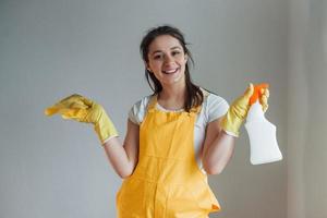 casalinga nel giallo uniforme in piedi con pulizia spray per finestre al chiuso. Casa rinnovamento concezione foto