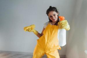 casalinga nel giallo uniforme in piedi con pulizia spray per finestre al chiuso. Casa rinnovamento concezione foto