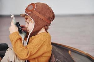 poco ragazzi nel retrò pilota costume avere divertimento e seduta nel valigia in casa a giorno foto