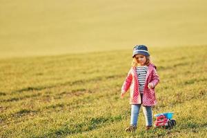 carino poco ragazza passeggiate con giocattolo auto su il bellissimo campo a soleggiato giorno foto