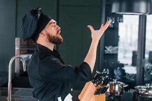 lato Visualizza di professionale giovane capocuoco cucinare nel uniforme quello in piedi su il cucina foto