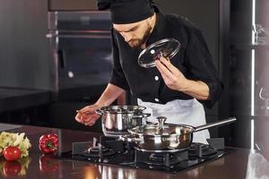 utilizzando attrezzatura. professionale giovane capocuoco cucinare nel uniforme Lavorando su il cucina con verdure foto