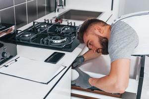 giovane professionale idraulico nel grigio uniforme Lavorando su il cucina foto