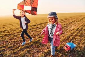 Due poco ragazze amici avere divertimento insieme con aquilone e giocattolo auto su il campo a soleggiato giorno foto