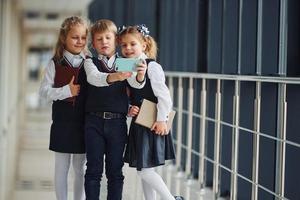 scuola bambini nel uniforme insieme con Telefono e fabbricazione autoscatto nel corridoio. concezione di formazione scolastica foto