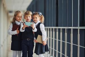 scuola bambini nel uniforme insieme con Telefono e fabbricazione autoscatto nel corridoio. concezione di formazione scolastica foto