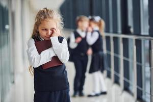 poco ragazza prende vittima di bullismo. concezione di molestie. scuola bambini nel uniforme insieme nel corridoio foto