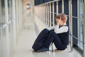 ragazzo nel uniforme seduta solo con sensazione triste a scuola. concezione di molestia foto