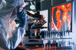 scienziato nel bianca protettivo uniforme vicino viene visualizzato con dati lavori con coronavirus e sangue tubi nel laboratorio foto