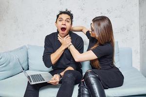 uomo con Riccio capelli e donna quello nel nero Abiti seduta con il computer portatile in casa e avere divertimento foto