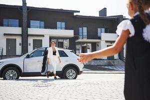 madre con figlia nel scuola uniforme all'aperto vicino bianca auto foto