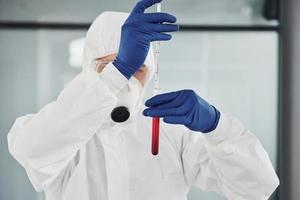 maschio medico scienziato nel laboratorio cappotto, difensiva occhiali e maschera lavori con test tubo con sangue dentro di esso foto