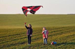 Due poco ragazze amici avere divertimento insieme con aquilone e giocattolo auto su il campo a soleggiato giorno foto