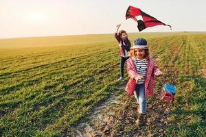 Due poco ragazze amici avere divertimento insieme con aquilone e giocattolo auto su il campo a soleggiato giorno foto