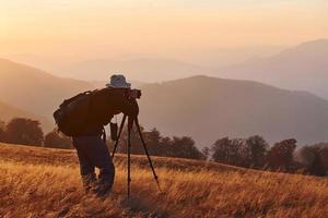 maschio fotografo in piedi e Lavorando a maestoso paesaggio di autunno alberi e montagne di il orizzonte foto