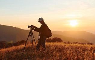 maschio fotografo in piedi e Lavorando a maestoso paesaggio di autunno alberi e montagne di il orizzonte foto