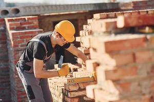 le misure di mattone parete. costruzione lavoratore nel uniforme e sicurezza attrezzatura avere lavoro su edificio foto