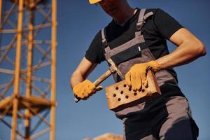 detiene mattone e attrezzo nel mani. costruzione lavoratore nel uniforme e sicurezza attrezzatura avere lavoro su edificio foto