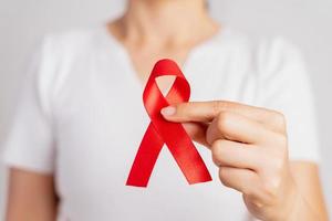 primo piano donna mano che tiene il nastro rosso hiv, nastro di consapevolezza della giornata mondiale contro l'AIDS. concetto di assistenza sanitaria e medicina. foto