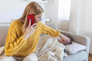 giovane donna controllo temperatura con mano di poco malato figlio. madre chiamata un' medico per sua malato ragazzo malato bambino dire bugie su letto sotto coperta con donna controllo febbre su fronte di mano. foto