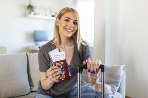 viaggio durante covid-19 pandemia. sorridente donna con passaporto, aria Biglietti e covid passaporto a moderno casa nel soleggiato giorno. foto