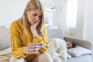 madre a casa e misurare un' temperatura su sua malato bambino. malato poco ragazzo seduta su letto. il ragazzo ha un' testa dolore e febbre. il madre è confortante il ragazzo. foto