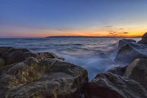 tramonto al di sopra di il mare con spruzzo onde su il rocce foto