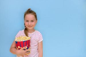 poco ragazza con un' grande bicchiere di Popcorn su un' blu sfondo con copia spazio foto