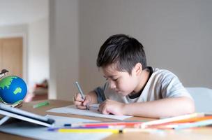 formazione scolastica concetto, scuola ragazzo utilizzando grigio colore penna disegno o schizzi su carta, ritratto ragazzo ubicazione su tavolo fare compiti a casa nel vivente stanza, bambino godere arte e mestiere attività a casa su fine settimana foto