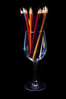 multicolore matite nel un' vino bicchiere e un' benna. selettivo sfocato un' gruppo di colorazione matite nel un' vino bicchiere su il isolato bianca o nero sfondo , moderno arte. moderno foto