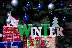 il iscrizione inverno a partire dal un' albero su un' nuovo anni. su il abete rosso rami contro il sfondo di un' neve copertina siamo nuovo anni blu, bianca palle con abete rosso coni e un' scatola con un' regalo. Natale foto