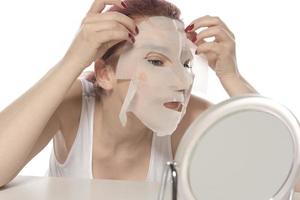 viso cura e bellezza trattamenti. donna con un' foglio idratante maschera su sua viso isolato su bianca sfondo foto