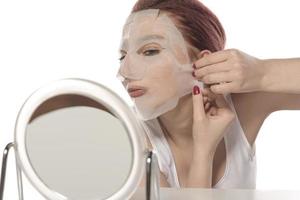 viso cura e bellezza trattamenti. donna con un' foglio idratante maschera su sua viso isolato su bianca sfondo foto