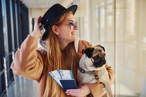 giovane femmina passeggeri nel caldo Abiti Tenere Biglietti e carino cane nel mani nel aeroporto sala foto