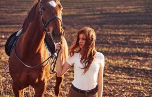 giovane donna in piedi con sua cavallo nel agricoltura campo a soleggiato giorno foto