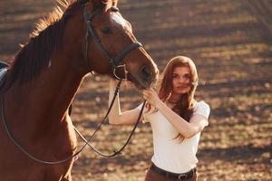 giovane donna in piedi con sua cavallo nel agricoltura campo a soleggiato giorno foto