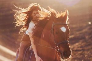 giovane donna nel protettivo cappello con sua cavallo nel agricoltura campo a soleggiato giorno foto